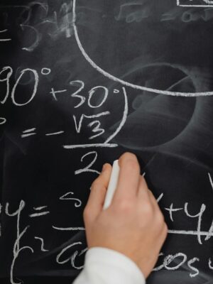 Hand writing complex math equations on a blackboard in a classroom setting.