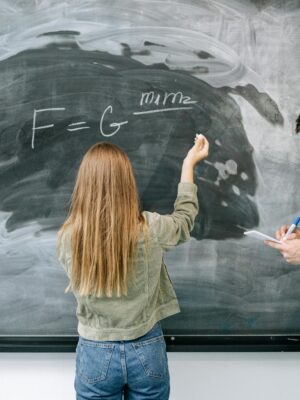 Two students discuss and solve a physics equation on the chalkboard.